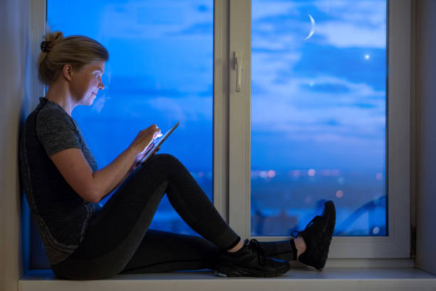 Smiling woman sitting on sill and using digital tablet.
