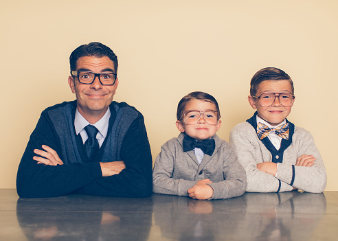 A father and his sons in nerd outfits are cheesy smiling at the camera. These boys love bonding over being smart together. The father is raising his sons to be the next generation of intellectual geniuses.