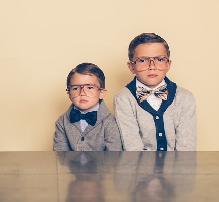 Two nerd boys are staring with a blank looks on their faces. Before video games you dealt with boredom by being bored. The boys are wearing bow ties and eyeglasses waiting for something exciting to happen.