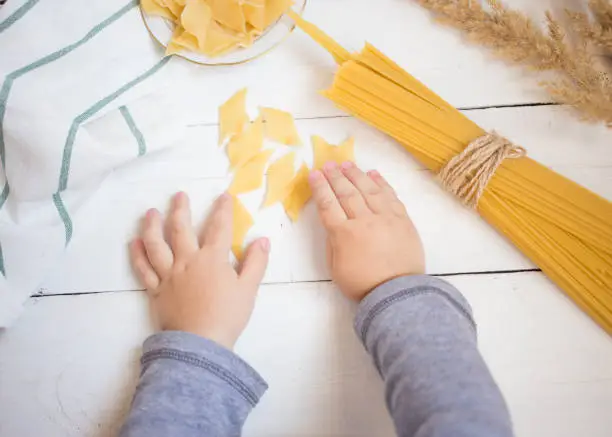 little baby's hands holding pasta on the white wooden table