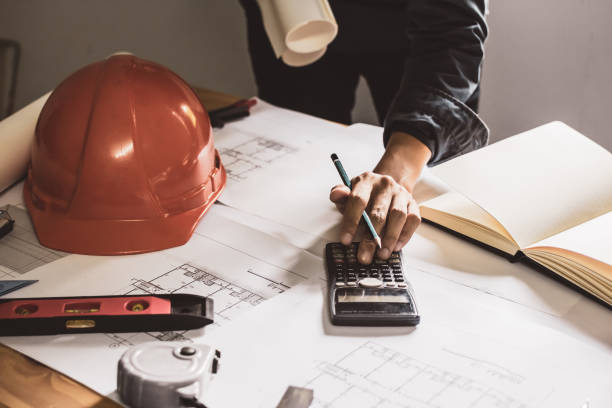 istock Concept architects,engineer Using a calculator to calculate the structure. equipment On desk with a blueprint in office. Vintage, Sunset light.Selective Focus 992598156