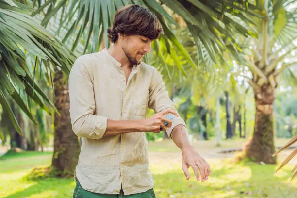 Young man spraying mosquito insect repellent in the forrest, insect protection.