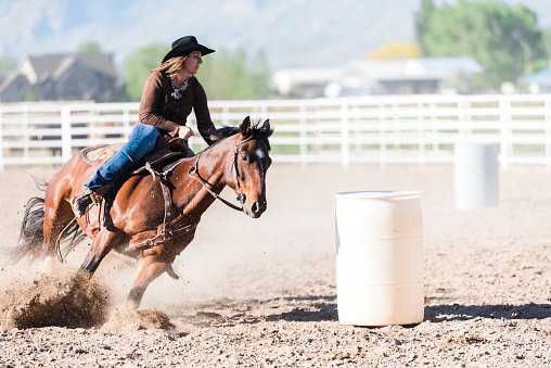 Woman practicing barrel racing in arena on ranch moving at speed