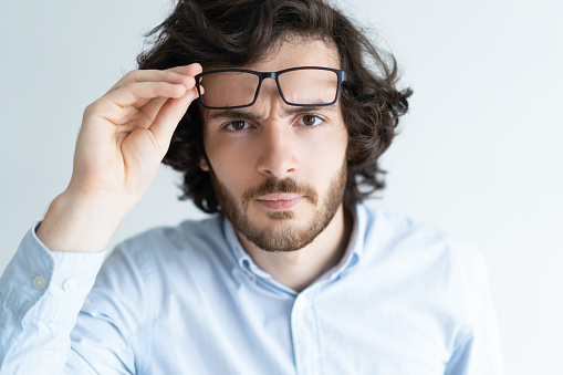 Surprised attractive young man staring at camera. Black-haired guy taking glasses off. Surprising news concept. Isolated front view on white background.