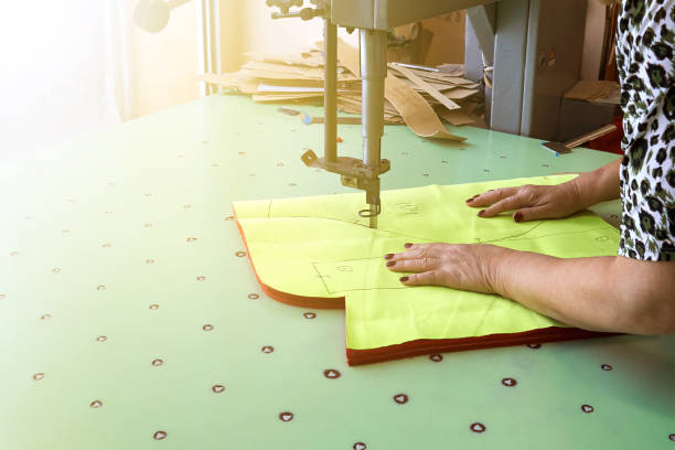 istock Female worker on a sewing manufacture uses electric cutting fabric machine. 992705642