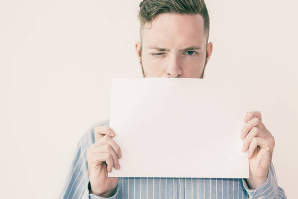 istock Man Holding Blank Sheet of Paper ad Winking 992710240