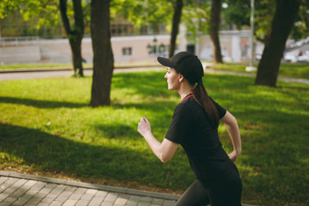istock Young concentrated athletic beautiful brunette girl in black uniform and cap training doing sport exercises running looking straight on path in city park outdoors. Fitness, healthy lifestyle concept. 992710638