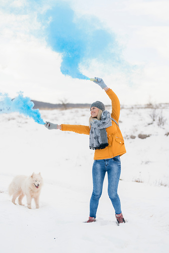 Beautiful, young woman and her samoyed dog having fun with a smoke bomb, on the snowy mountain.