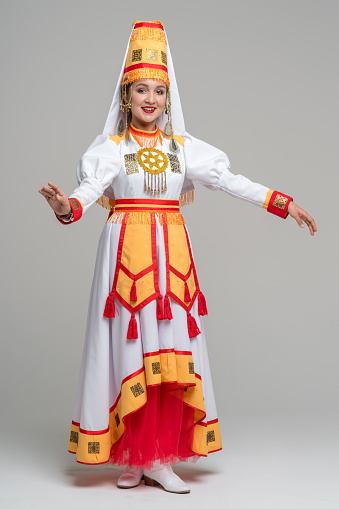 Nice young woman dressed in women's traditional clothes and jewelry which are recreated according to medieval samples of the Mari people. The young woman shows a folk dance. She is smiling looking at the camera. Studio shooting on white background