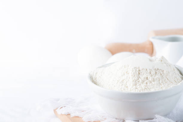 Baking ingredients. White background. Ingredients and tools to make a cake. Flour, milk, eggs, rolling pin, wooden spoons, jar. Copy space. Bakery. Baking concept