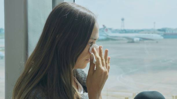 Young sad woman is crying at airport with airplane on the background Young sad woman is sitting on the window sill at airport, crying and wipes tears away with airplane on the background wiping tears stock pictures, royalty-free photos & images