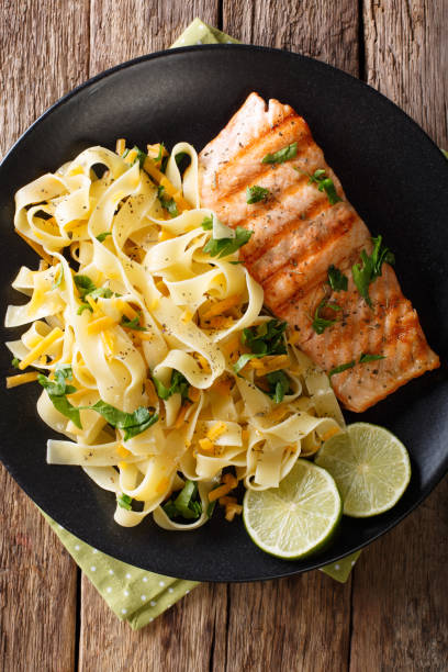 istock Pasta fetuccini with cheese cheddar and grilled salmon with herbs on a plate close-up. vertical top view 992754792