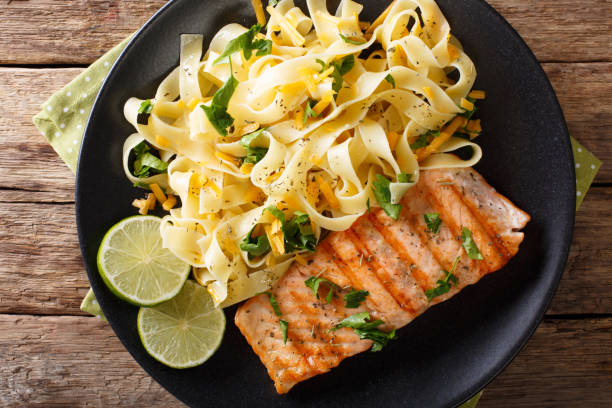 istock Pasta fetuccini with cheese cheddar and grilled salmon with herbs on a plate close-up. Horizontal top view 992756864