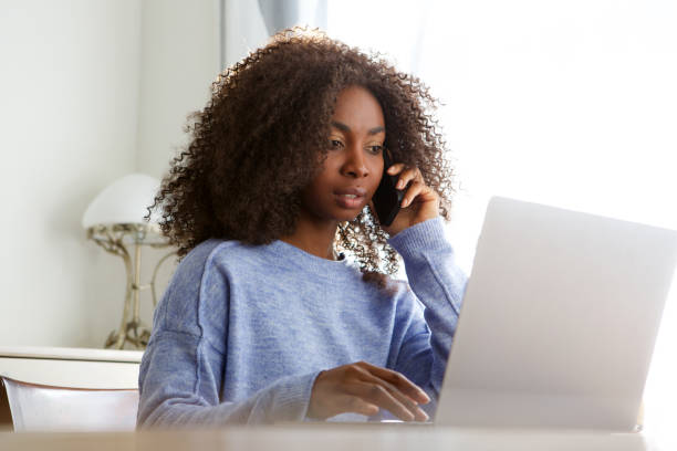 istock young black woman talking on mobile phone and using laptop 992757802