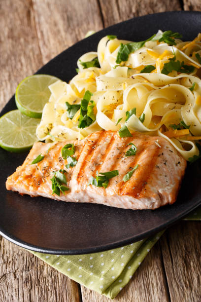 istock Pasta fetuccini with cheddar and grilled salmon on a plate close-up. vertical 992758824