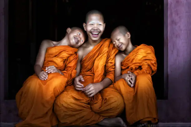 Photo of Three Thai Buddhist novices sitting together at temple door feeling happy and smile