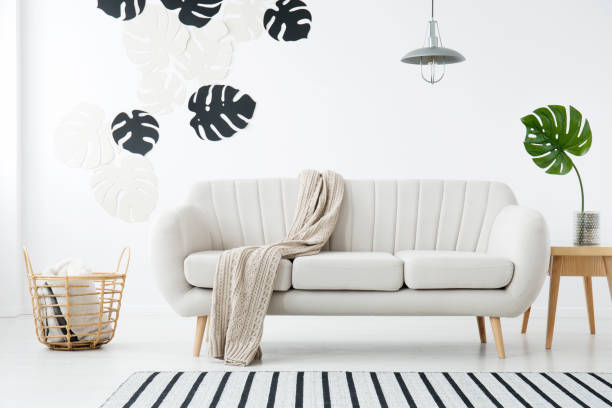 istock Blanket on sofa next to basket in white living room interior with monstera leaf on table. Real photo 992777554