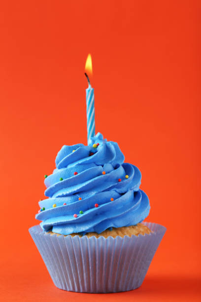 istock Tasty cupcake with candle on orange background 992790980