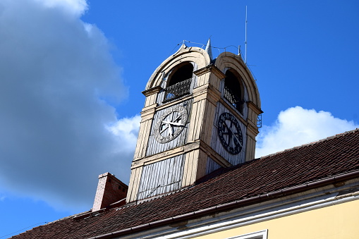 A close up on a historic clock tower with working wooden clock and wooden frame on the top of a roof of a municipal office with clouds covering a part of the blue sky