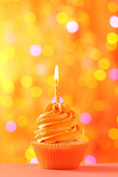 istock Tasty cupcake with candle on lights background 992791320