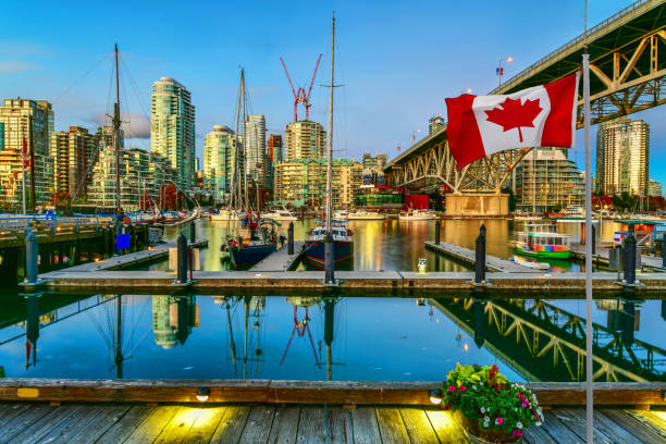 Granville island at twilight in Vancouver,Canada Canadian flag in front of view Ferry boat docked in Granville island at twilight in Vancouver,Canada granville island stock pictures, royalty-free photos & images