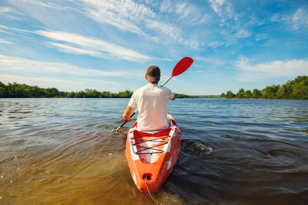 Happy adult man kayaking on the river at a sunny morning and enjoying life - water sport on the weekend. Wide angle, back view.
