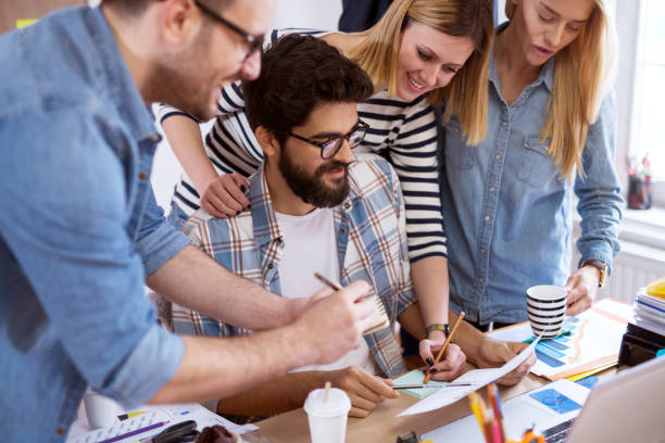 istock Group of young businessmen is trying to develop new ideas and are writing down the notes in their notebooks and are drinking coffee. 992799810