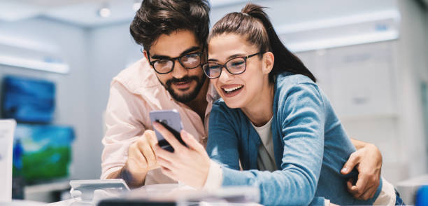 istock Young beautiful couple is trying out test phone model in a tech store. 992807200
