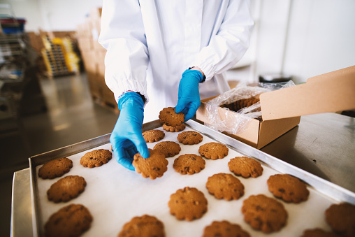 A worker in blue sterile gloves is packing brown cookies .