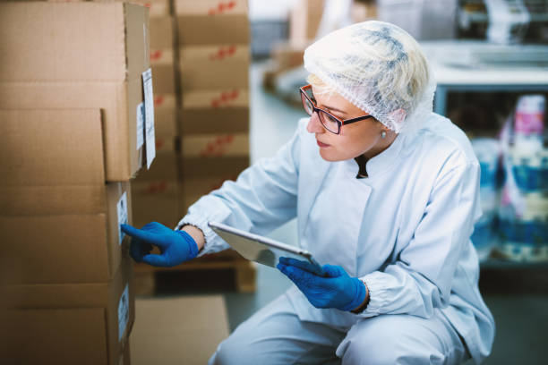 istock Young focused female worker in sterile cloths is checking the stack of boxes and comparing numbers with those on a tablet. 992810514