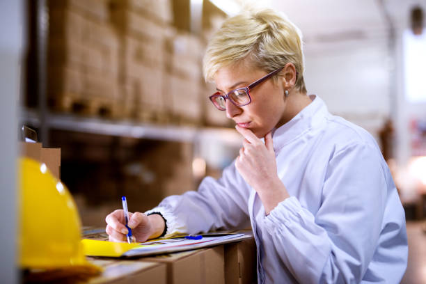 istock Young beautiful focused female worker is checking statistics papers on stack of boxes . 992810914