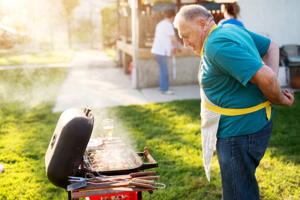 istock Elderly pleased man is tieing his apron while proudly checking if his grilled meat is ready. 992814808