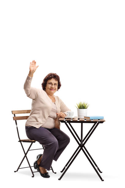 istock Senior lady sitting at a coffee table and waving at the camera 992815436