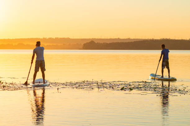 istock Men, friends sail on a SUP boards in a large river during sunrise 992815632