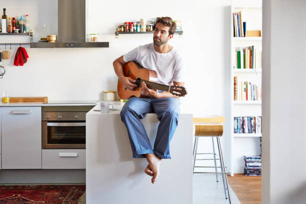 Shot of a handsome young man playing the guitar in the morning at home
