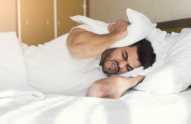 istock Young man trying to sleep covering ears with pillow 992829942