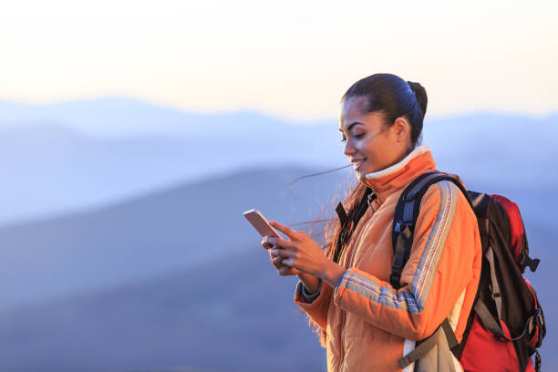 sorrindo de pedestrianismo feminino usando telefone inteligente na montanha superior - sunrise asia china climbing - fotografias e filmes do acervo