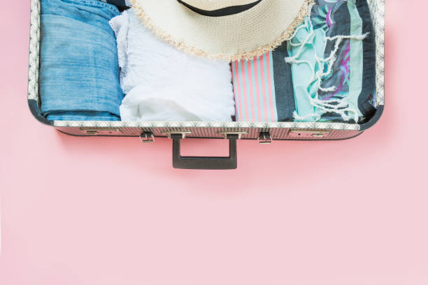 istock Open suitcase with female clothes for trip on pastel pink. Top view with copy space. Summer concept travel. 992837210