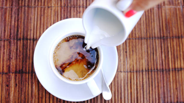 вид на заливку ручья молока в чашку эспрессо на деревянном столе. - coffee nobody macro directly above стоковые фото и изображения