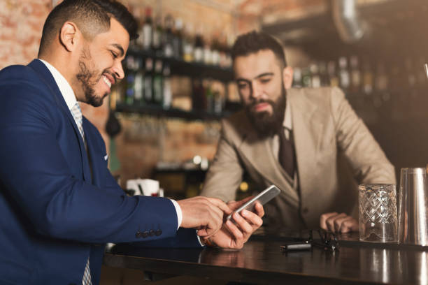 istock Businessman showing information on phone to barman 992848166
