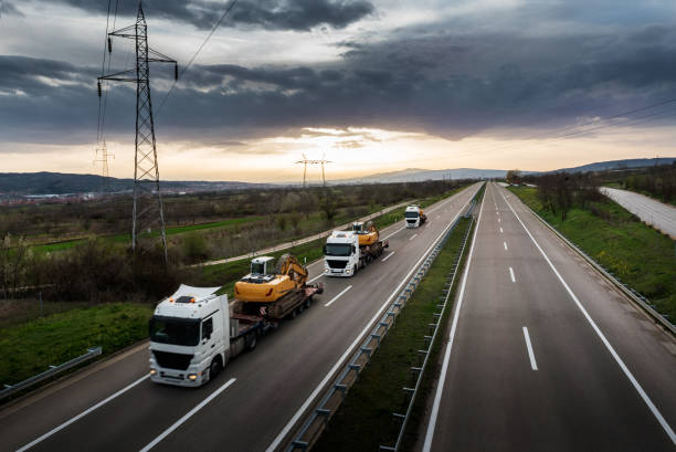 Tow Trucks in a row carrying Construction Machines Excavators Tow Trucks in a convoy or caravan carrying Construction Machines Excavators along the Highway construction machinery stock pictures, royalty-free photos & images