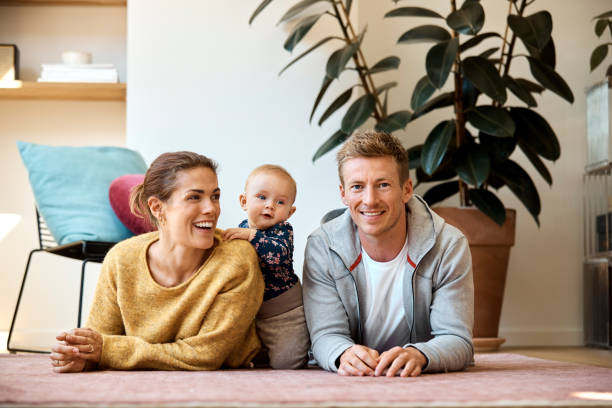 famiglia felice di tre persone sdraiata sul tappeto a casa - floor two parent family couple home interior foto e immagini stock