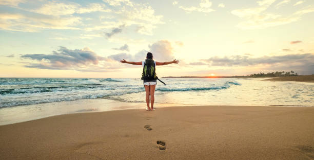 istock Woman backpacker greeting a sunset at the ocean coast 992856104