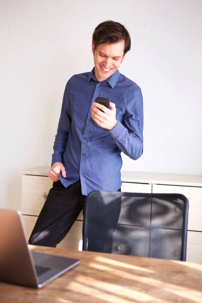 istock smiling man standing in home office holding mobile phone 992863324