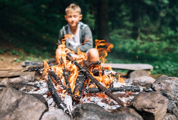 istock Boy sits near campfire. Summer camping time 992870478