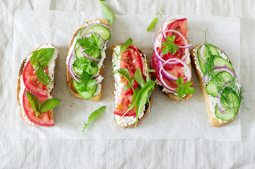 Bruschetta or sandwiches with tomatoes, cucumbers and cream cheese, decorated with greens. Selective focus