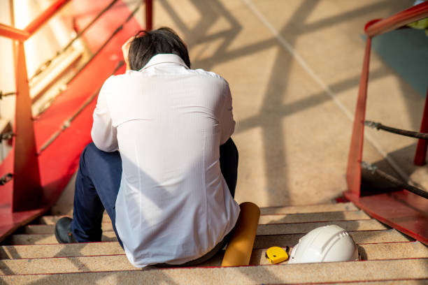 istock Engineer or Architect feeling stressed, worried and tired with his job while sitting on stair with protective safety helmet at construction site.  Problem and failure with construction project concept 992889880