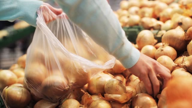 woman putting onion to bag at grocery store