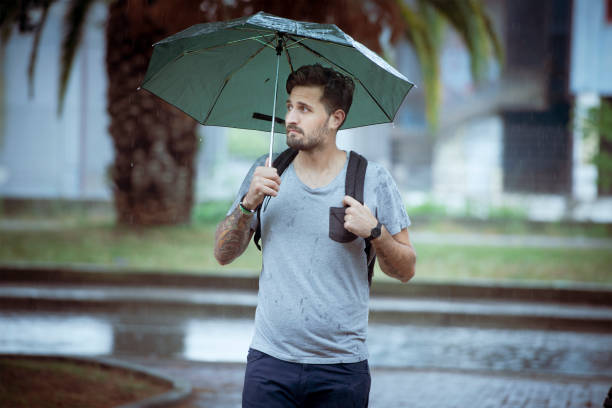 istock Young Adult Man Walking Under The Rain 992901964