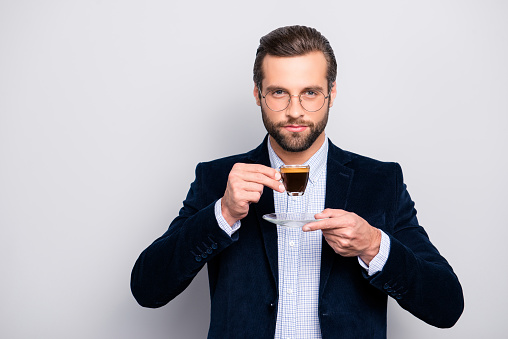 Portrait of chic handsome pleased delightful serious attractive dreamy wealthy elegant classy man smelling the aroma of fresh bitter coffee isolated on gray background copy-space